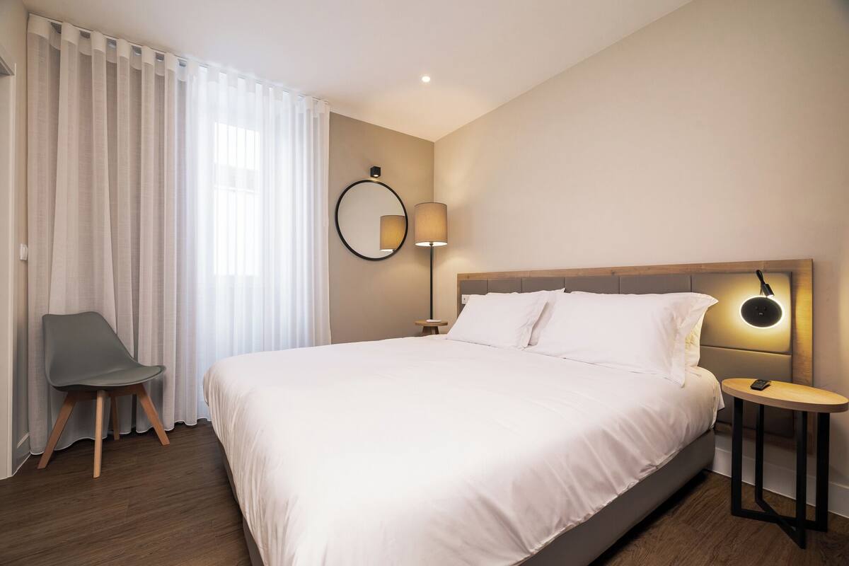 A hotel room with a large bed, a chair, a bedside table, and a lamp.