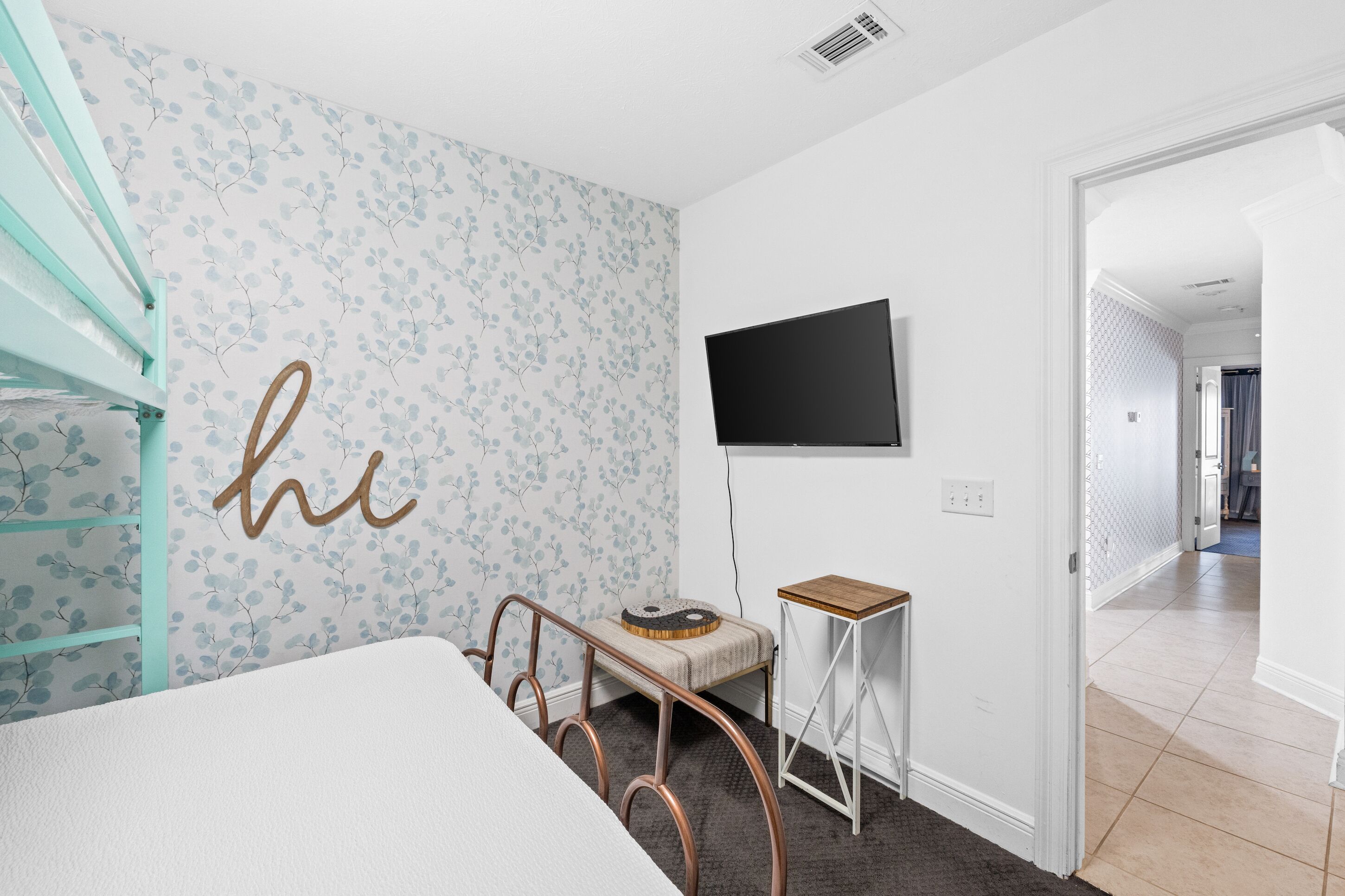 A bedroom with a bed, a small table, a TV, and a wall with a floral pattern.