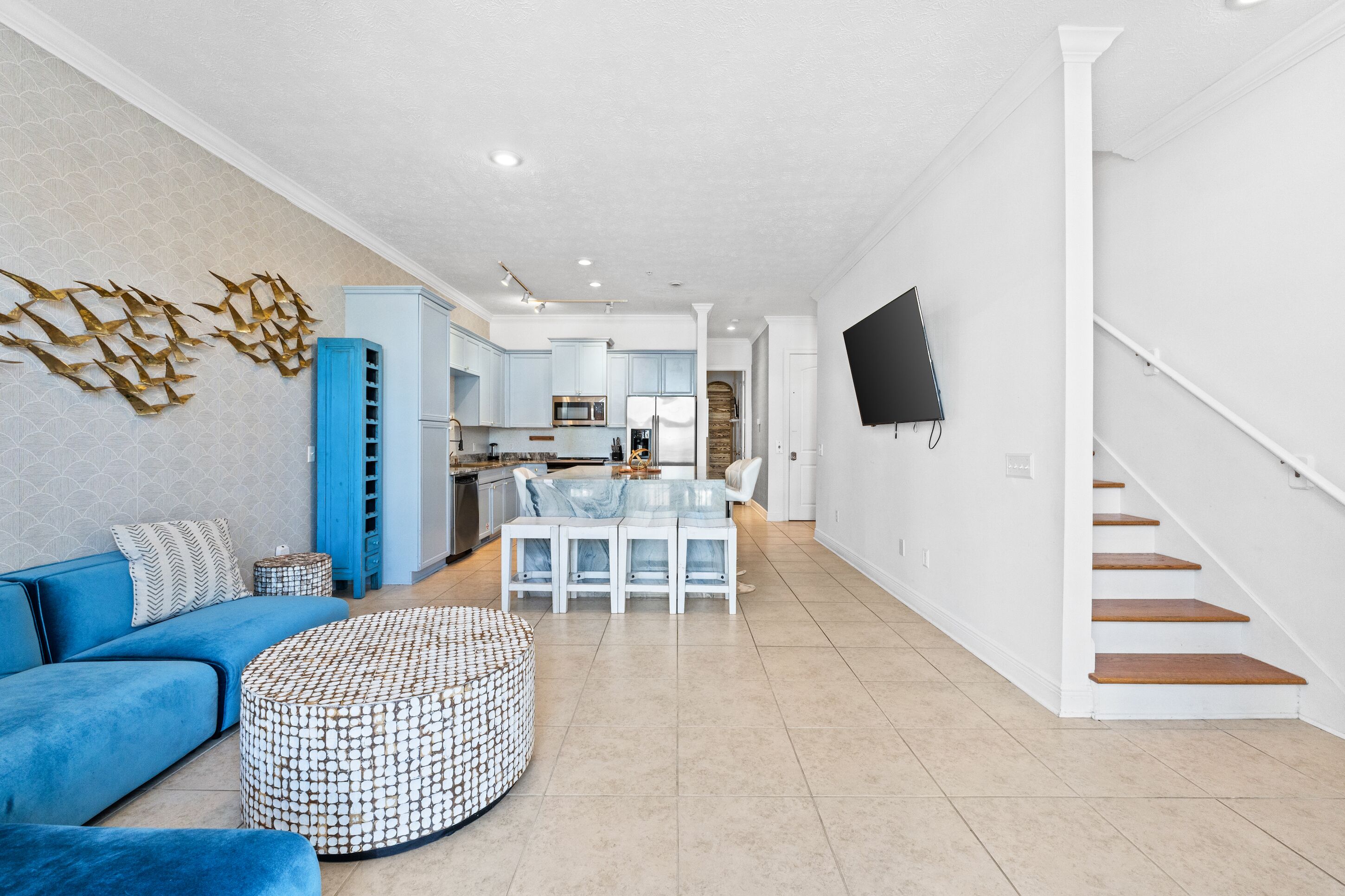 Un salon moderne avec un canapé bleu, un pouf à motifs et un coin repas doté d’une table en verre.