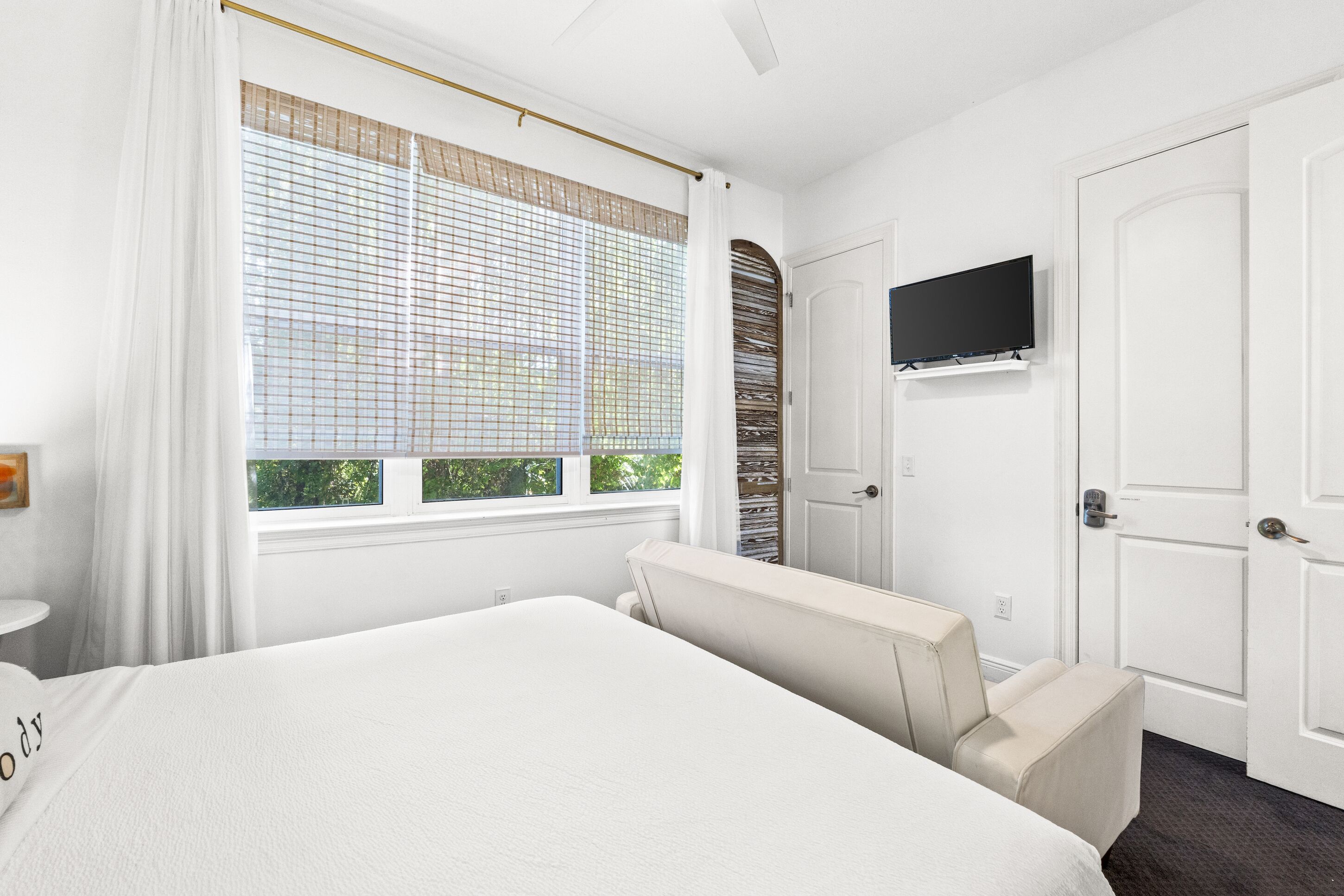 A hotel room with a bed, a TV mounted on the wall, a window with blinds, and a door.