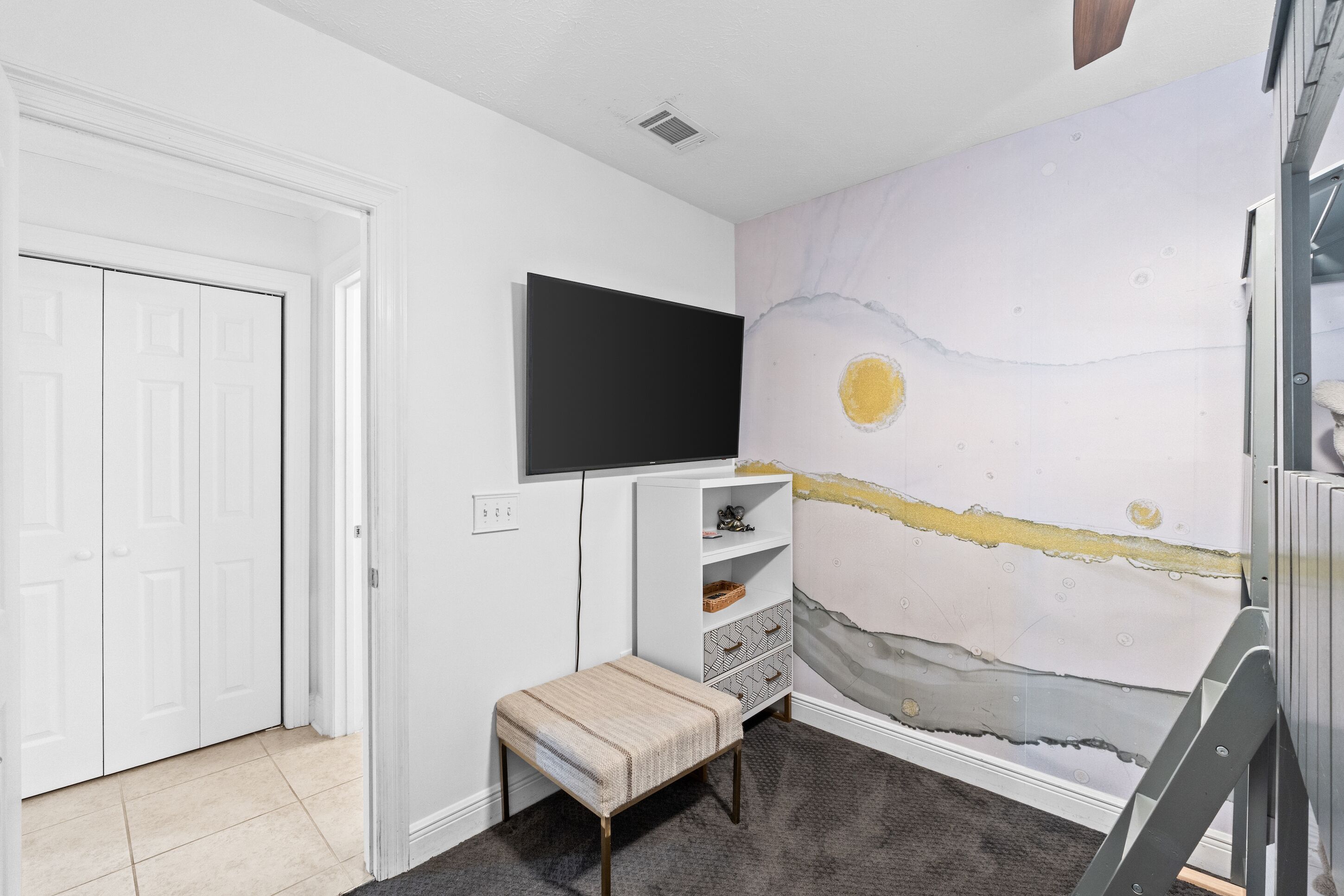 Una habitación con una puerta blanca, un televisor de pantalla plana montado en la pared, un banco y una pared pintada a medias.