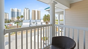 Parveke, jossa on rottinkituoli, valkoiset kaiteet ja näkymä korkeisiin rakennuksiin ja palmuille.