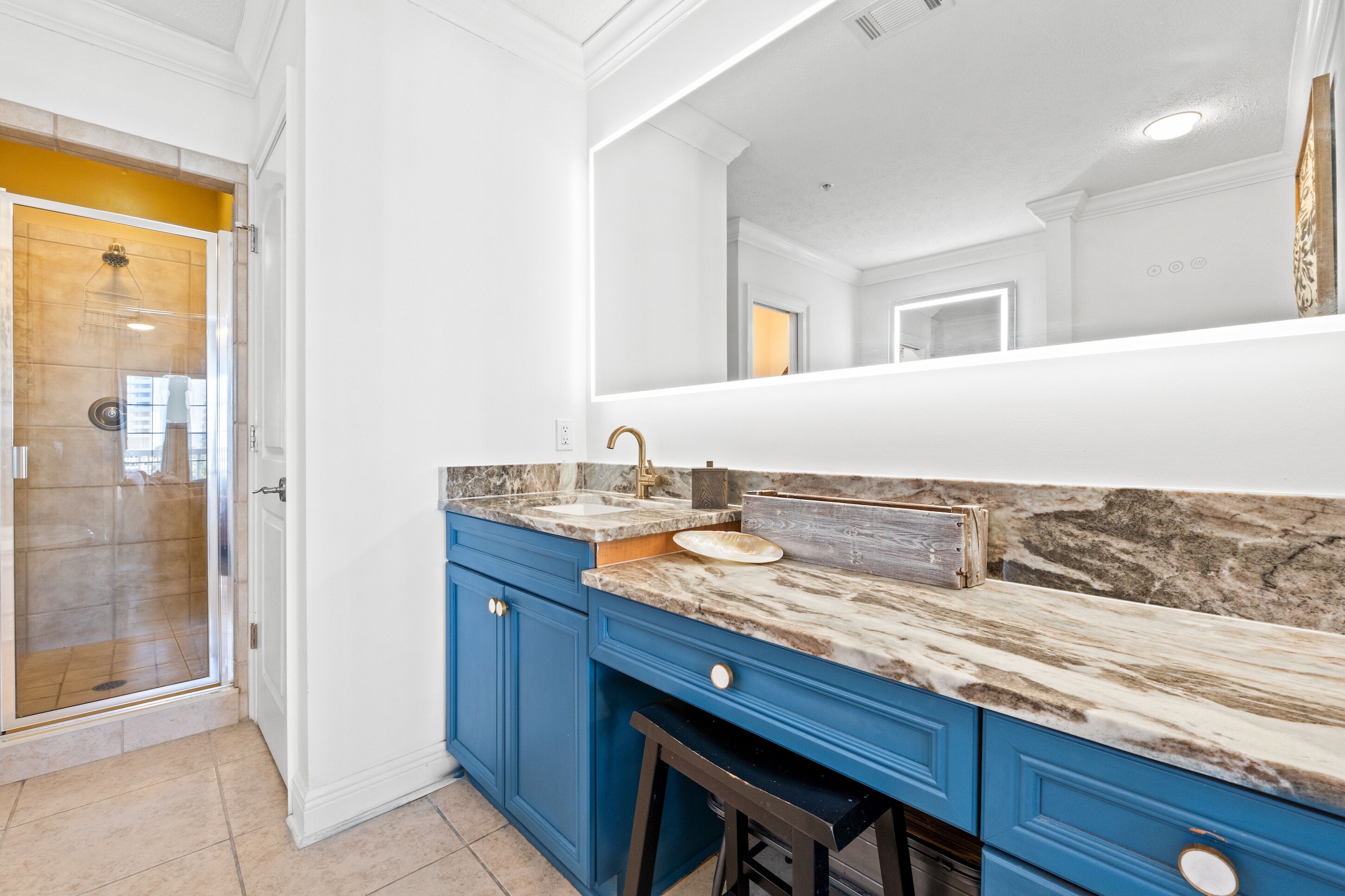 A modern bathroom with a marble countertop, blue cabinetry, and a large mirror.
