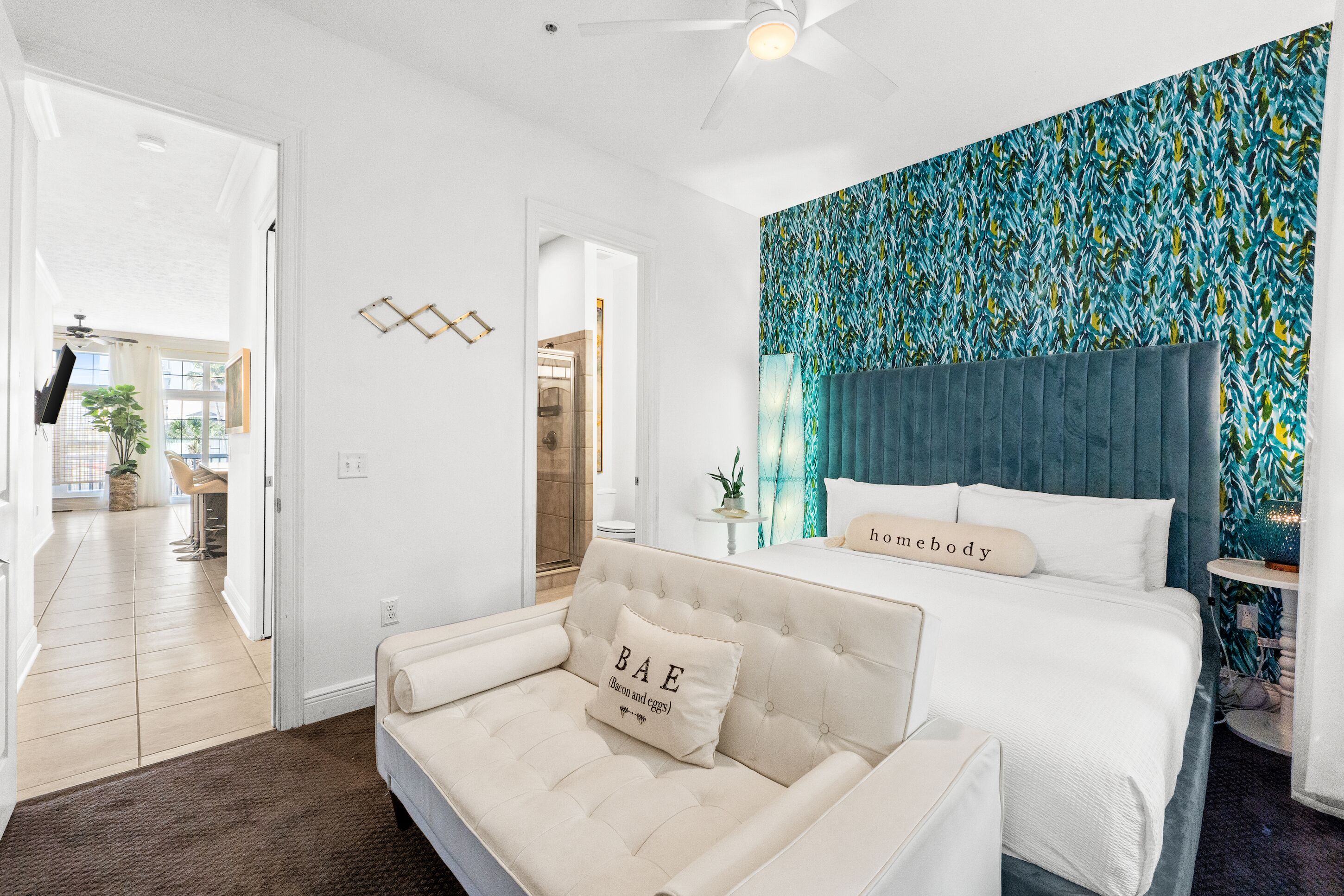 A modern bedroom with a large bed, a sofa, and a wall with a leafy pattern.
