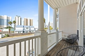 A balcony with white railings, two wicker chairs, and a view of tall buildings in the background.