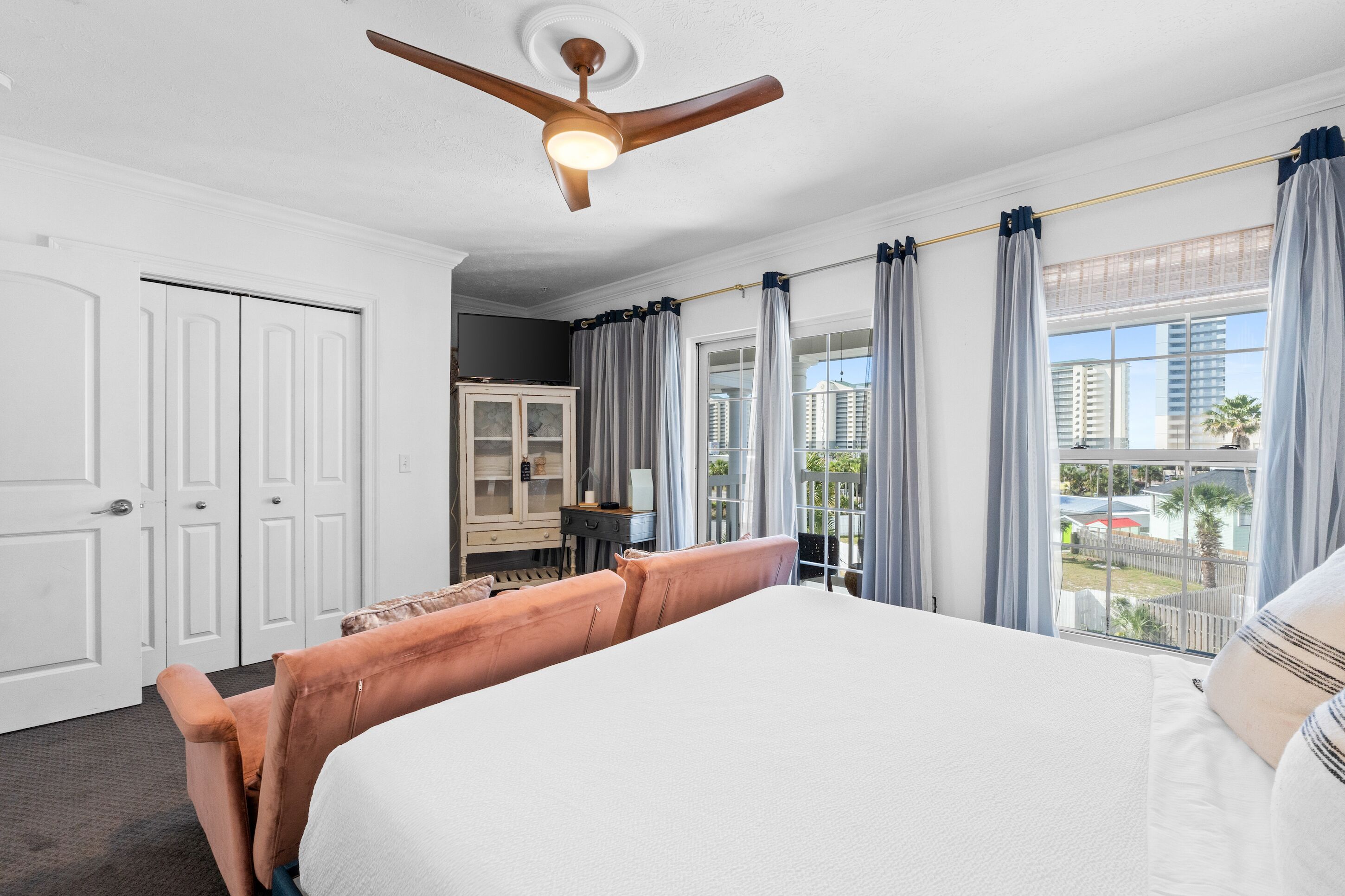Une chambre d’hôtel avec un grand lit, un ventilateur de plafond, une vue sur la ville et un bureau avec une chaise.