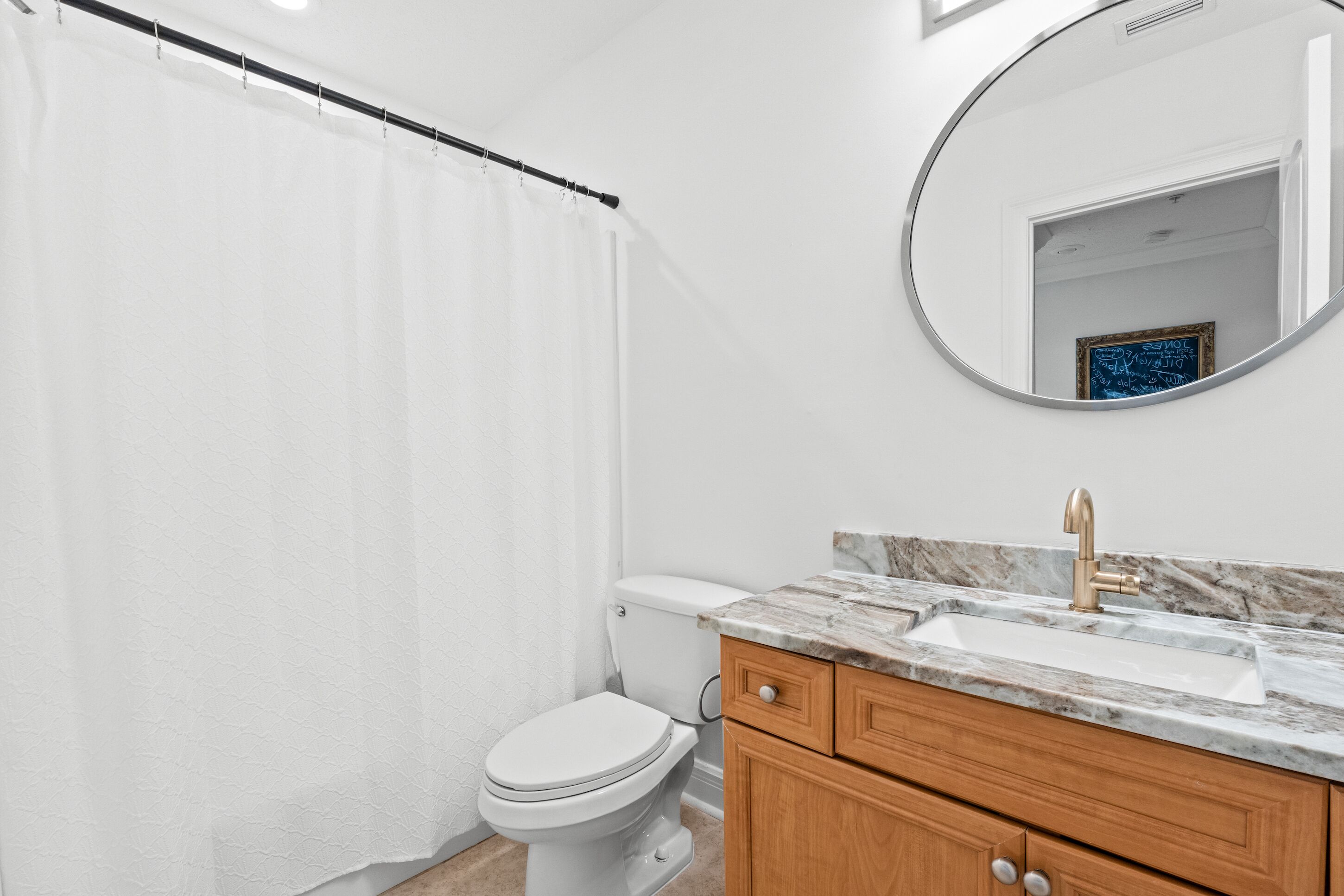 Une salle de bain avec des toilettes blanches, des meubles en bois, un comptoir en marbre et un rideau de douche.