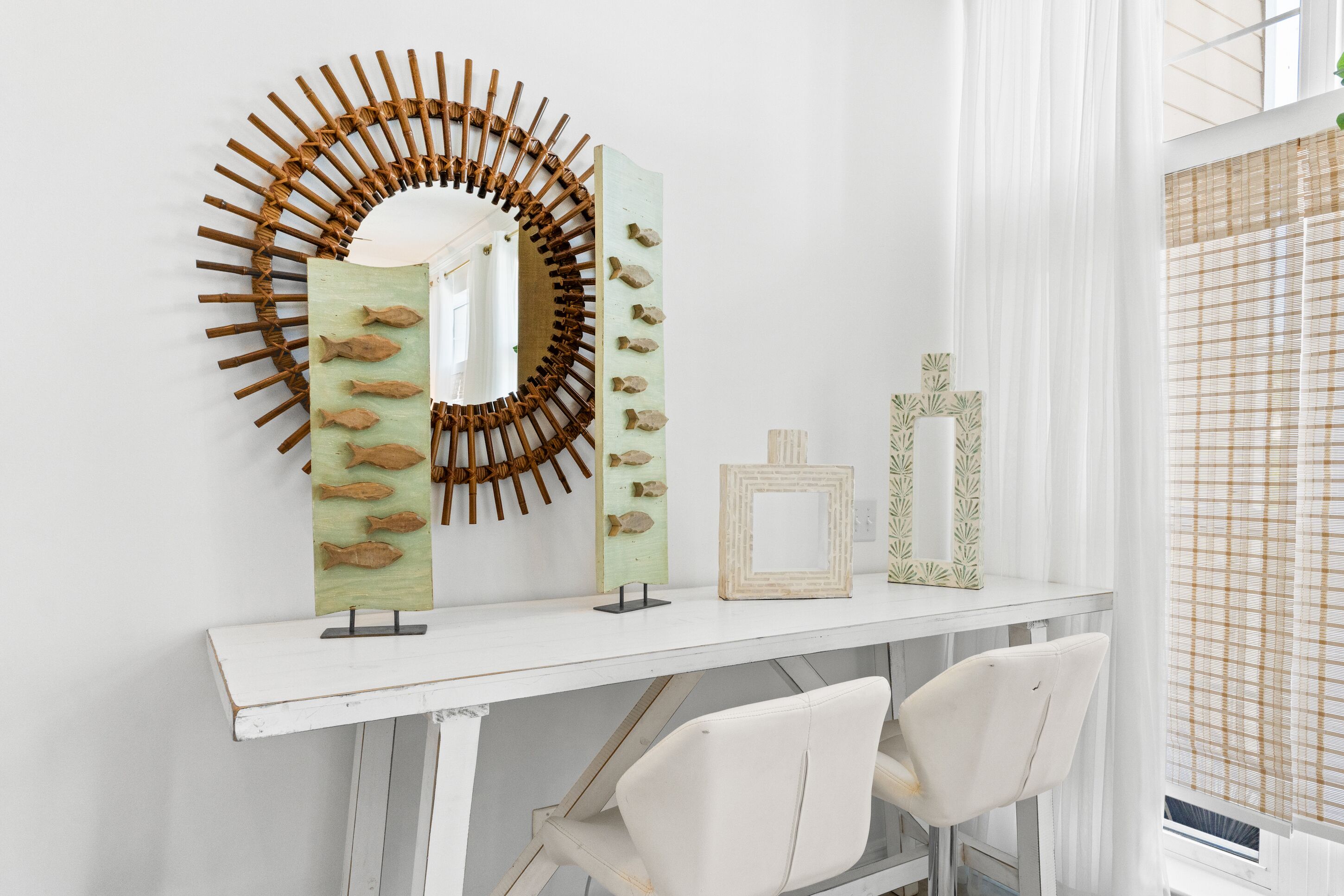 Une coiffeuse blanche avec un miroir, une décoration murale représentant des poissons en bois et un tableau encadré.