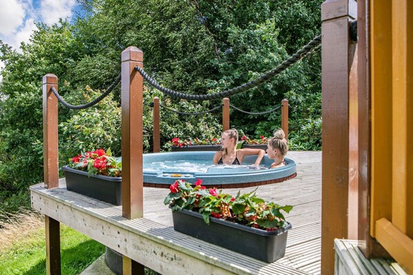 Ein Whirlpool auf einer Holzterrasse, umgeben von viel Grün.