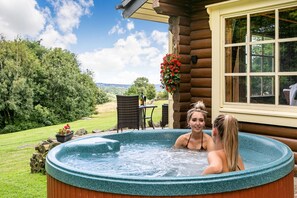 A hot tub in a log cabin with a view of the surrounding landscape.