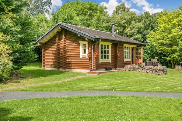 A log cabin with a sloped roof, a chimney, and a stone foundation.