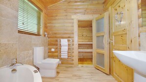 Baño de cabaña de madera con bañera, inodoro y zona de ducha.