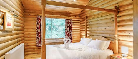 Un dormitorio tipo cabaña de madera con una cama con dosel, paredes de madera, una ventana con cortinas y una mesita de noche con lámpara.