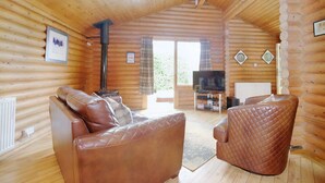 L'intérieur d'une cabane en rondins, avec un canapé, un fauteuil et une cheminée.