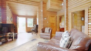 L’intérieur d’une cabane en rondins, avec un canapé en cuir, un téléviseur et un coin repas.
