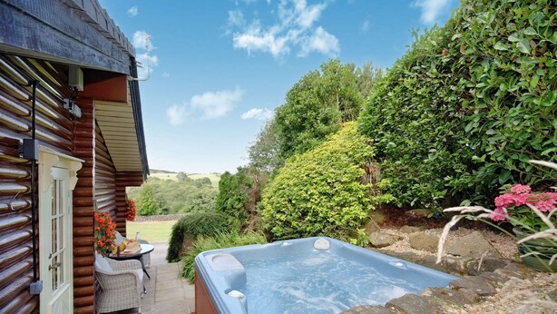 A hot tub in a garden with a wooden cabin in the background.