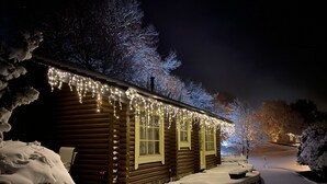 A log cabin with snow-covered exterior and a snow-covered driveway.