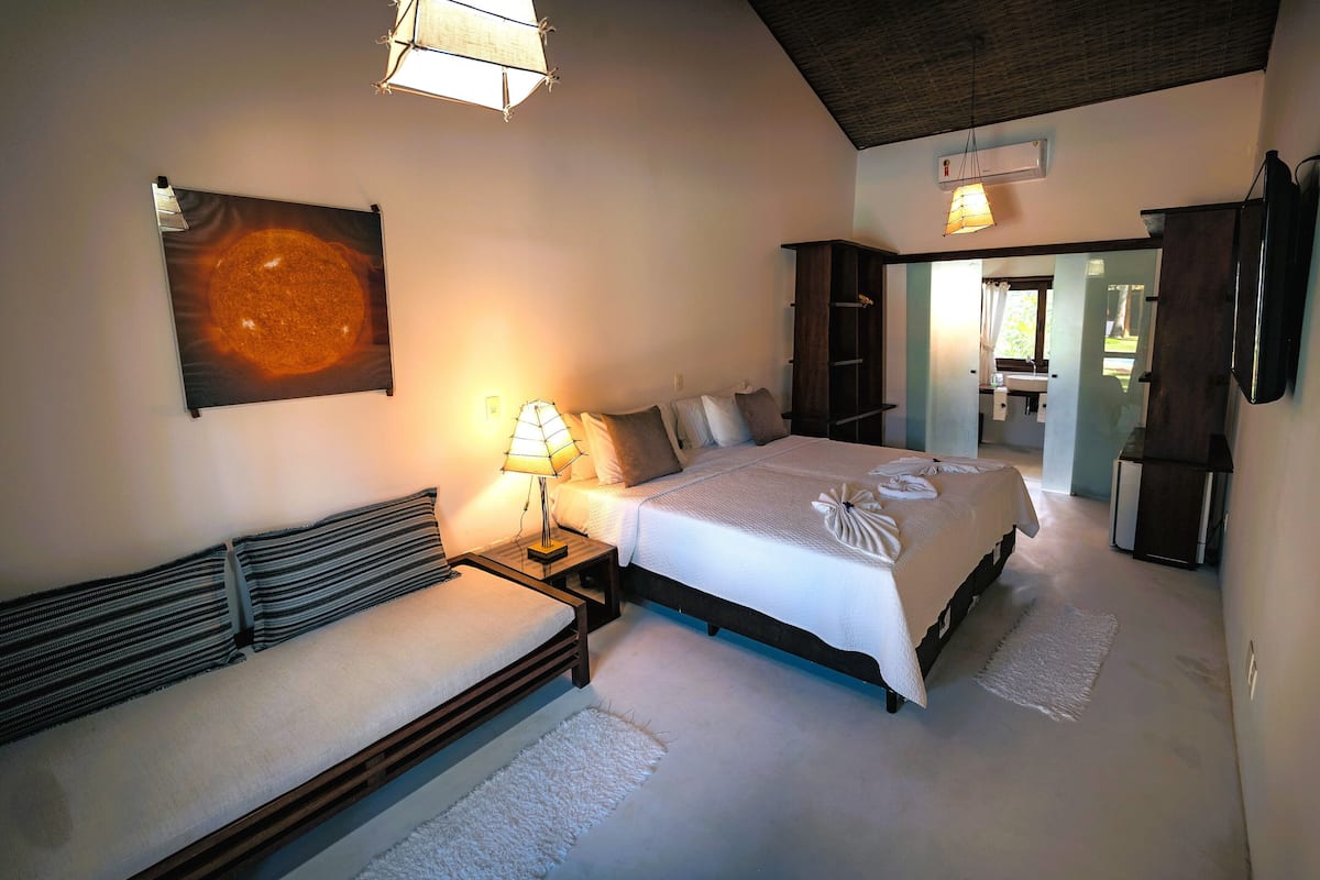 Un dormitorio con cama, mesitas de noche, un sofá y un amplio ventanal.