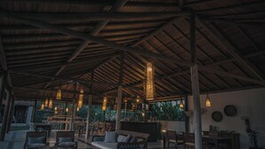 Un salón al aire libre con vigas de madera, asientos cómodos e iluminación colgante.