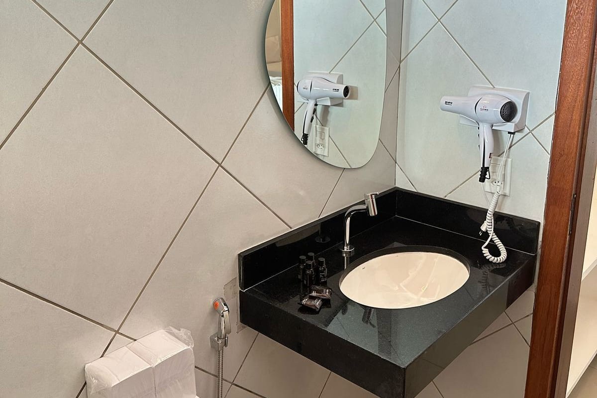 Un baño con un lavabo negro, un espejo redondo, un inodoro y una ducha.