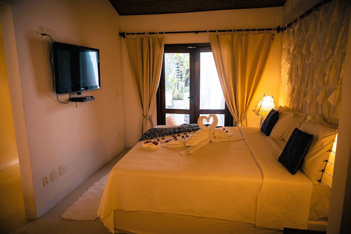 Un dormitorio con cama, cortinas, televisor y ventana.