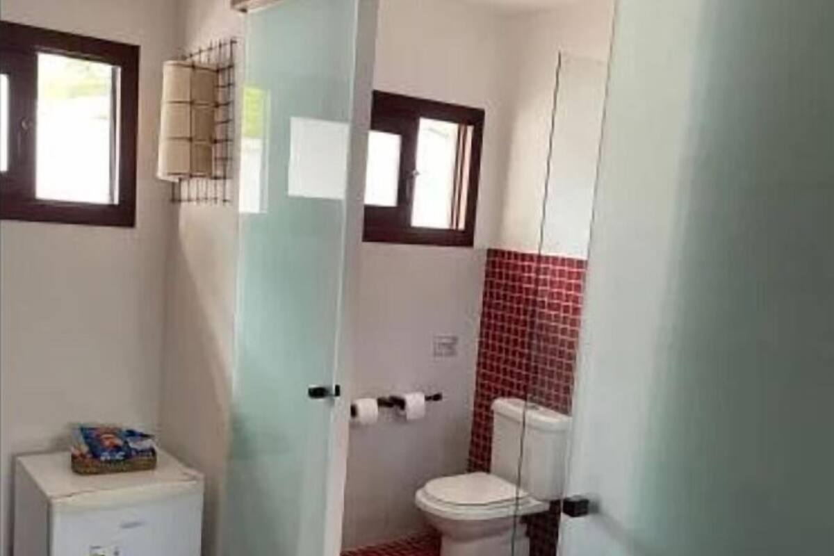 Un baño compacto con inodoro, un refrigerador pequeño y una ventana.
