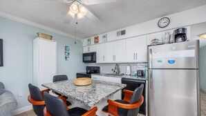 A compact kitchen with a dining table, chairs, a refrigerator, microwave, and a clock on the wall. - Sunset Sands Retreat #4-Beachfront–Sleeps 4 (Fort Walton)