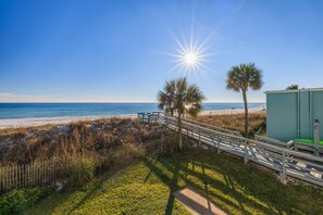 A beach view with a wooden walkway, palm trees, and a small building.