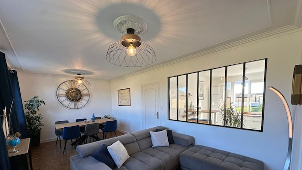 A modern living room with a sectional sofa, a dining area with a round table, and a large window offering a view of the outdoors. - CAP PLAGE 10 minutes' walk  (AUDIERNE)