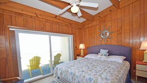 A wooden-paneled bedroom with a bed, a nightstand, a lamp, and a chair by the window. - Sea Edge 3-Oceanfront 36th St, W/D, AC, Free WIFI (Ocean City)