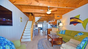 A spacious living area with a wooden ceiling, a green sofa, a coffee table, and a staircase leading to another room. - Sea Edge 3-Oceanfront 36th St, W/D, AC, Free WIFI (Ocean City)