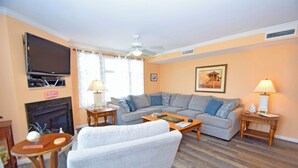 A living room with a sofa, armchairs, a coffee table, a fireplace, a television, and a ceiling fan.