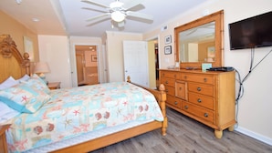 A bedroom with a bed, a dresser, a television, and a ceiling fan.
