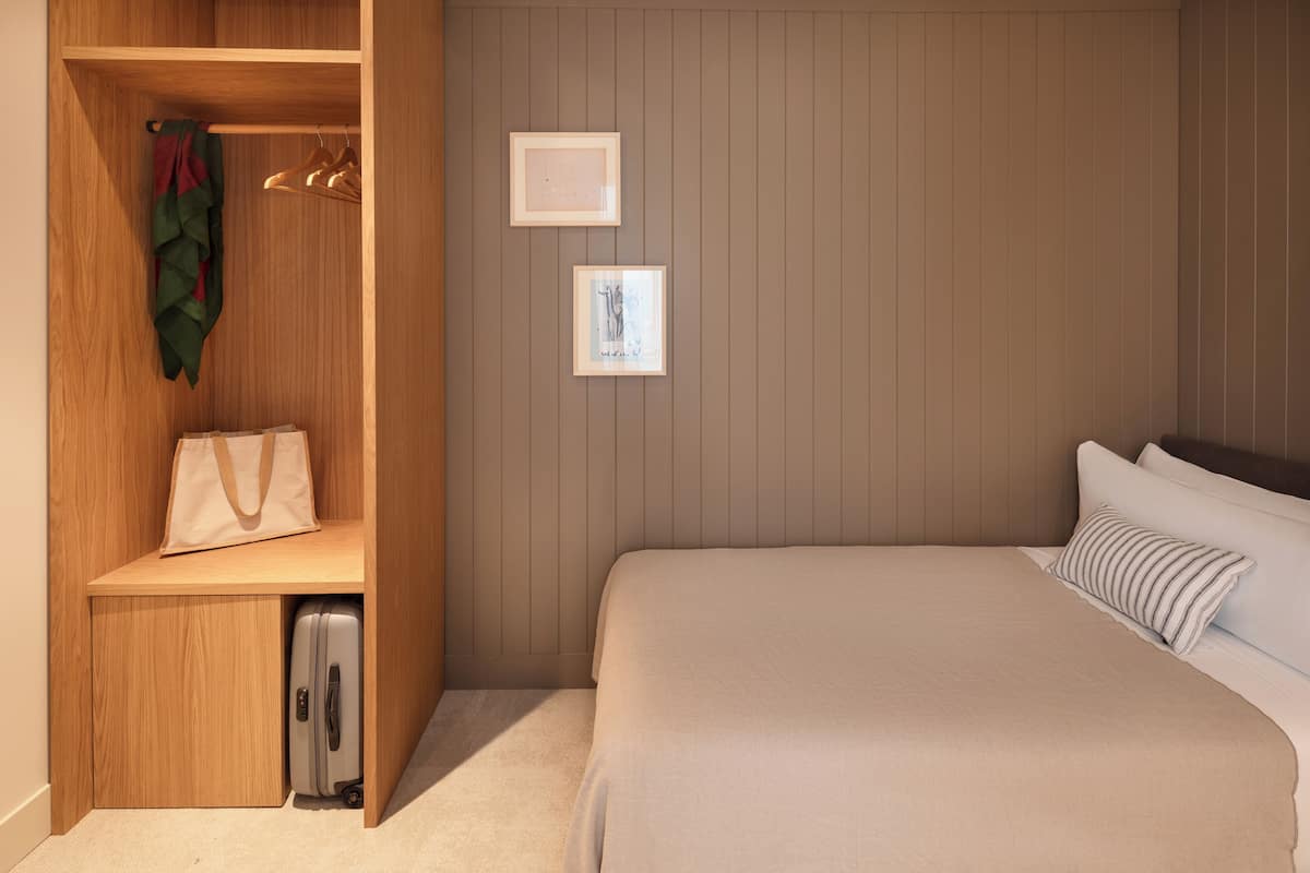 Een slaapkamer met een bed, een houten garderobe, een koffer en twee ingelijste foto's aan de muur.