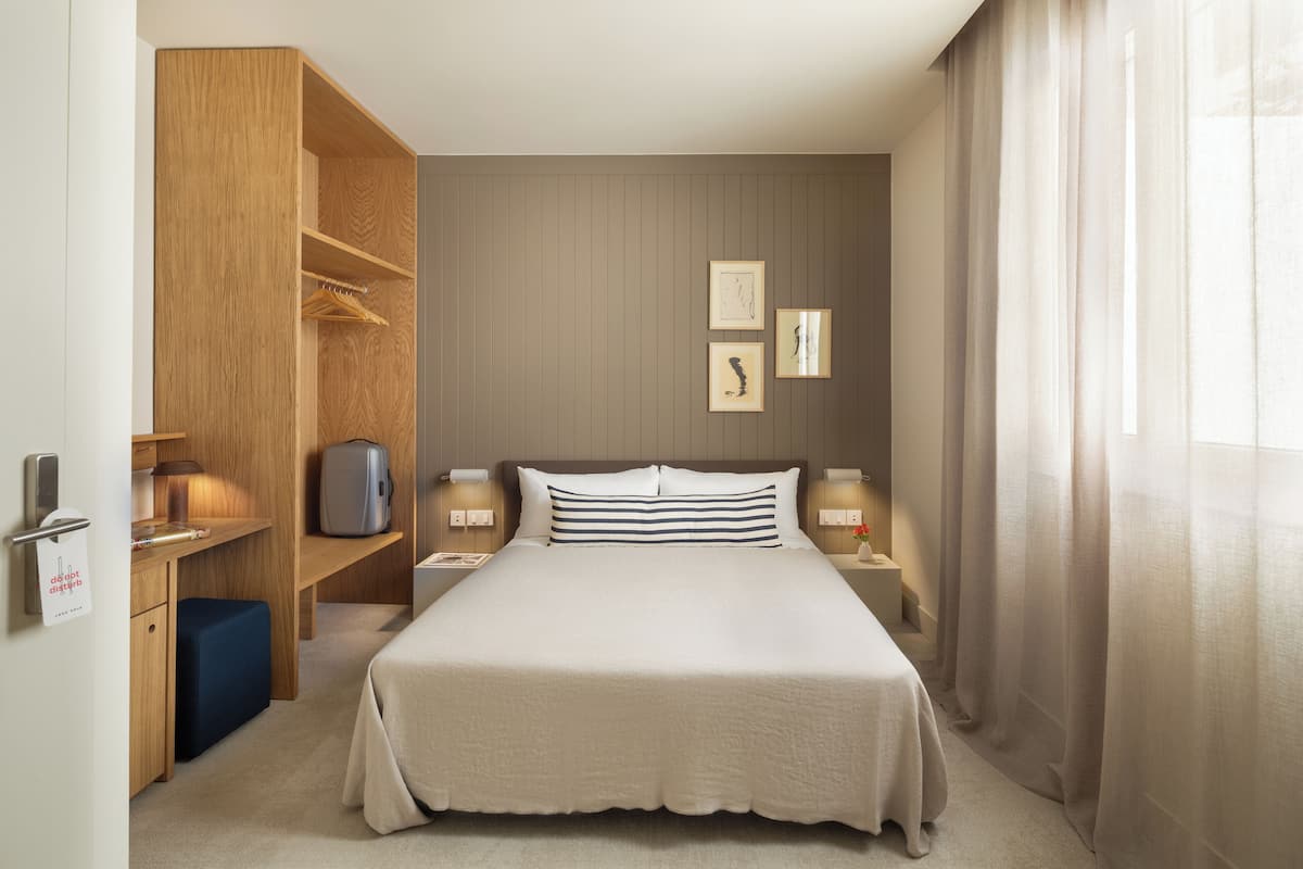Een keurig opgemaakt hotelkamer met een groot bed, nachtkastjes, een bureau en een kledingkast.