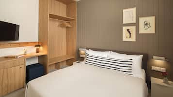 A hotel room with a large bed, wooden wardrobe, bedside tables, artwork on the wall, and a flat-screen TV.
