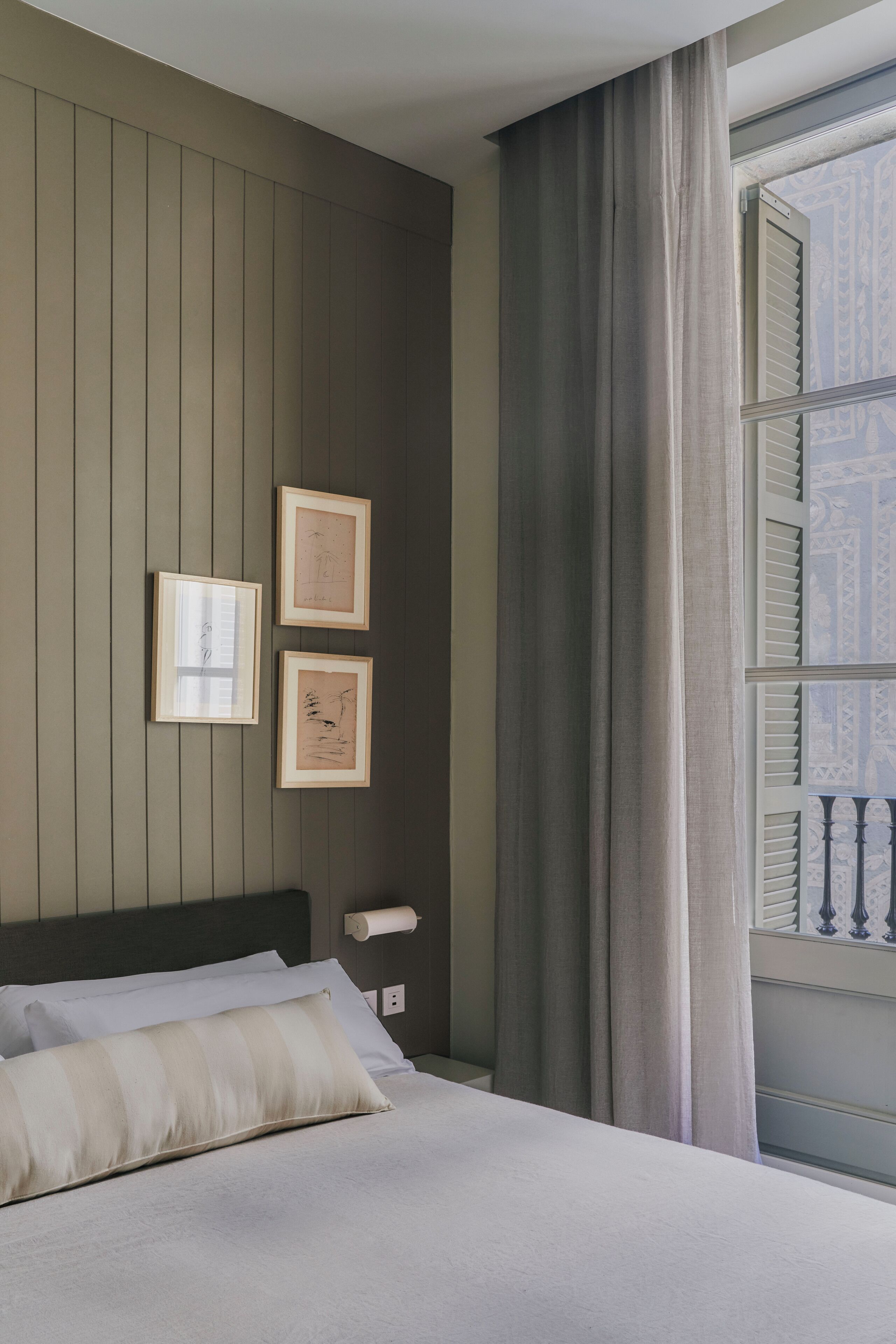 A bedroom with a bed, a window with curtains, and two framed pictures on the wall.