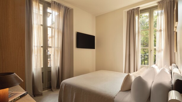 A hotel room with a bed, curtains, a flat-screen TV, and a window with a view. - Hotel Casa Teva (Barcelona)