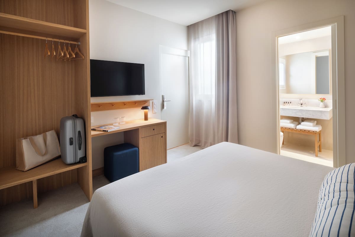 Hotelkamer met een bed, bureau met flatscreen televisie, kast en badkamer met spiegel en wastafel.