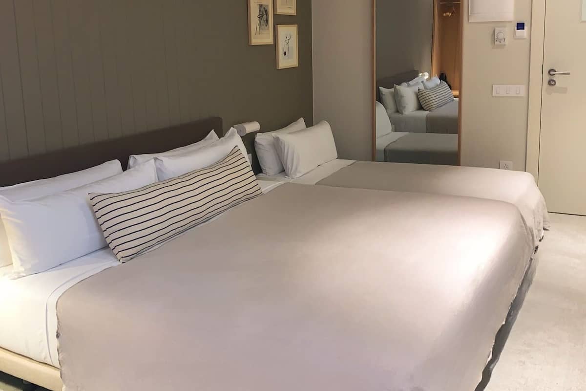 Een groot bed met witte lakens en gestreepte kussens, een houten hoofdbord en een spiegel aan de muur.
