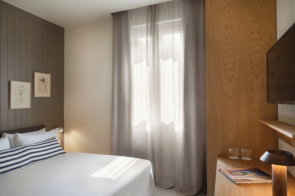 Een hotelkamer met een bed, een nachtkastje met glazen en een raam met gordijnen.