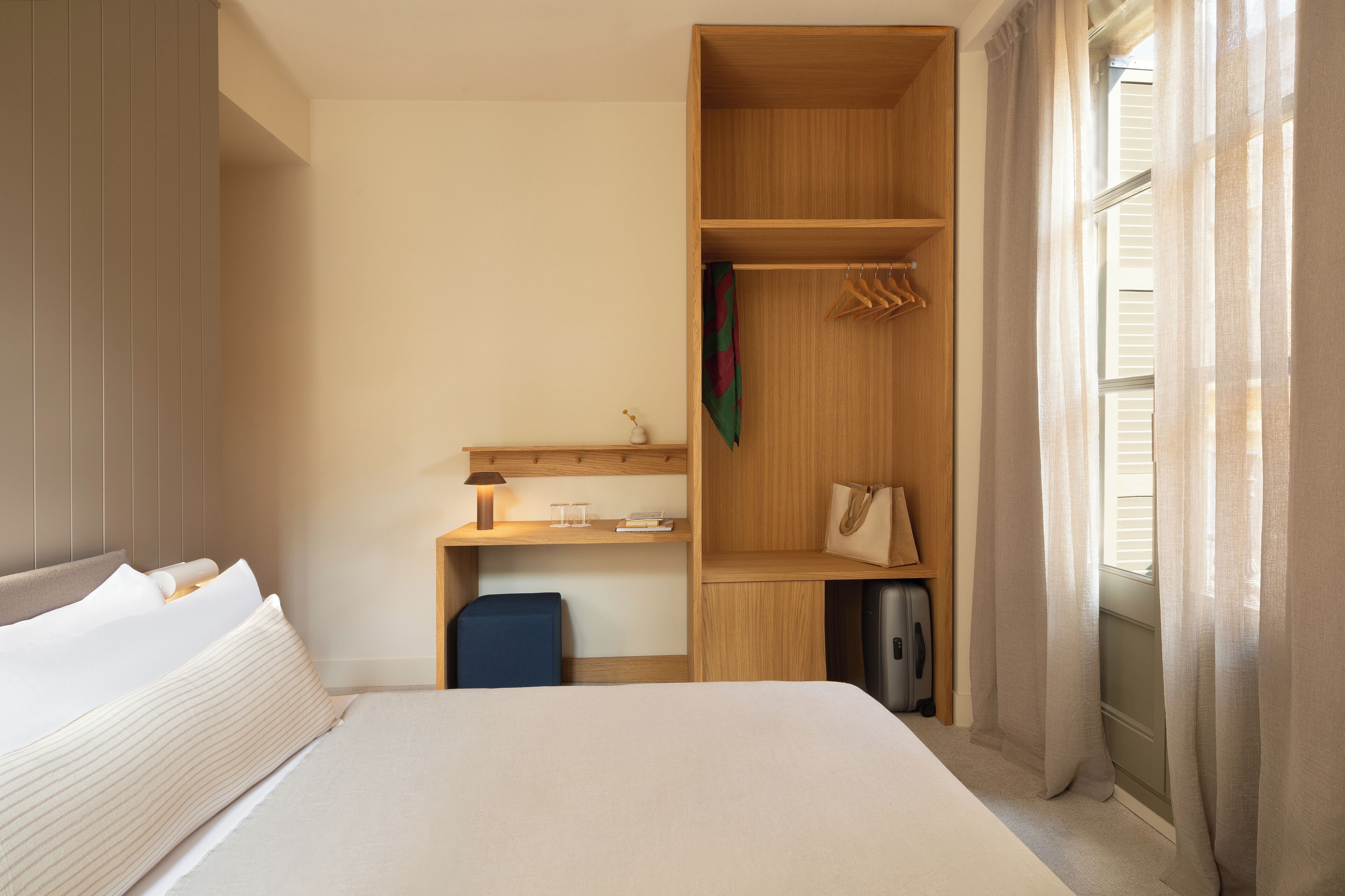 A hotel room with a bed, a desk, a wardrobe, and a window with curtains.