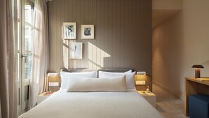 Una habitación de hotel con una cama grande, mesitas de noche con lámparas, un estante en la pared con fotografías enmarcadas y una ventana con cortinas.