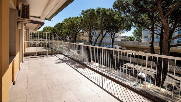 Ein Balkon mit Metallgeländer, Fliesenboden und Bäumen im Hintergrund.