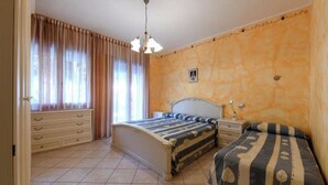 Ein Schlafzimmer mit Bett, Nachttisch, Kommode und einem Fenster mit Vorhängen.