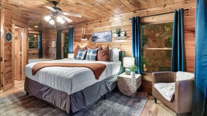 Un dormitorio de cabaña de madera con una cama, una mesita de noche, una silla y un ventanal grande.