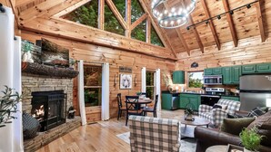 Interior acogedor de una cabaña con chimenea, pisos de madera, zona de comedor y cocina.