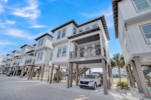 A row of modern, multi-story buildings with balconies and a white car parked in front. - Family Tides by Liquid Life (Gulf Shores)