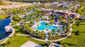 Vista aérea de um resort com várias piscinas, incluindo uma grande piscina central, e palmeiras ao redor.