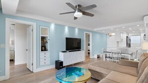 A modern living room with a ceiling fan, a glass coffee table, a sofa, and a TV on a white cabinet. - Royal Mauian, #511 2 Bedroom Condo by RedAwning (Kihei)